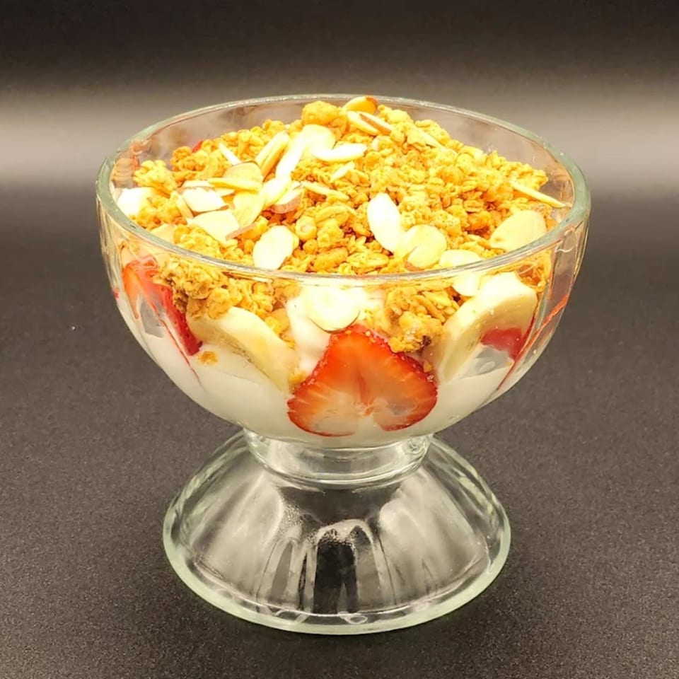 A glass bowl of yogurt parfait with granola, sliced strawberries, and bananas.