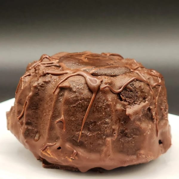 A rich, dark chocolate bundt cake with a glossy chocolate drizzle on a white plate.