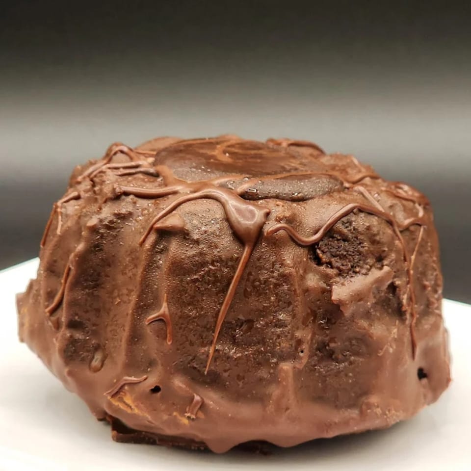 A rich, dark chocolate bundt cake with a glossy chocolate drizzle on a white plate.