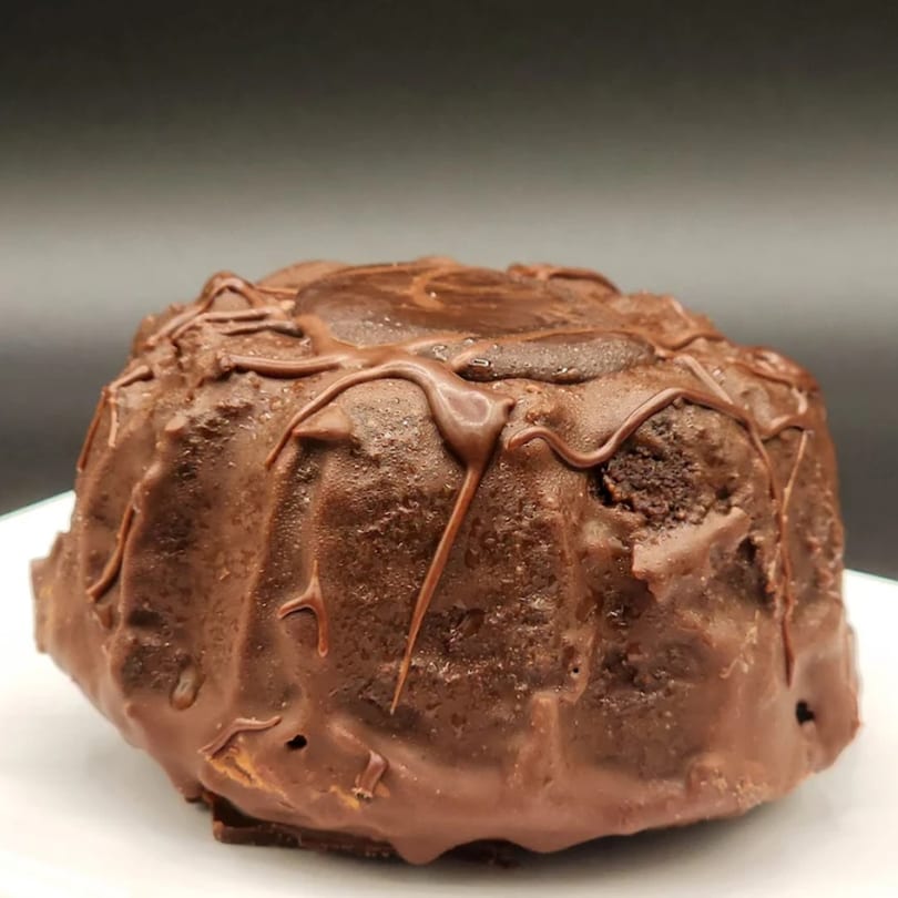 A rich, dark chocolate bundt cake with a glossy chocolate drizzle on a white plate.