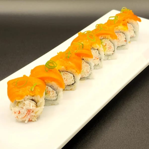 A long white plate holds eight sushi rolls topped with salmon and green onions.