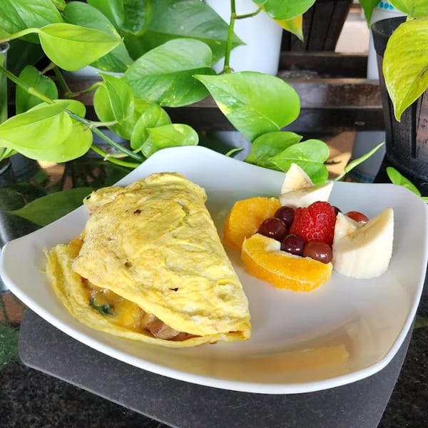A fluffy omelet with a side of fresh fruit including oranges, strawberries, grapes, and bananas.