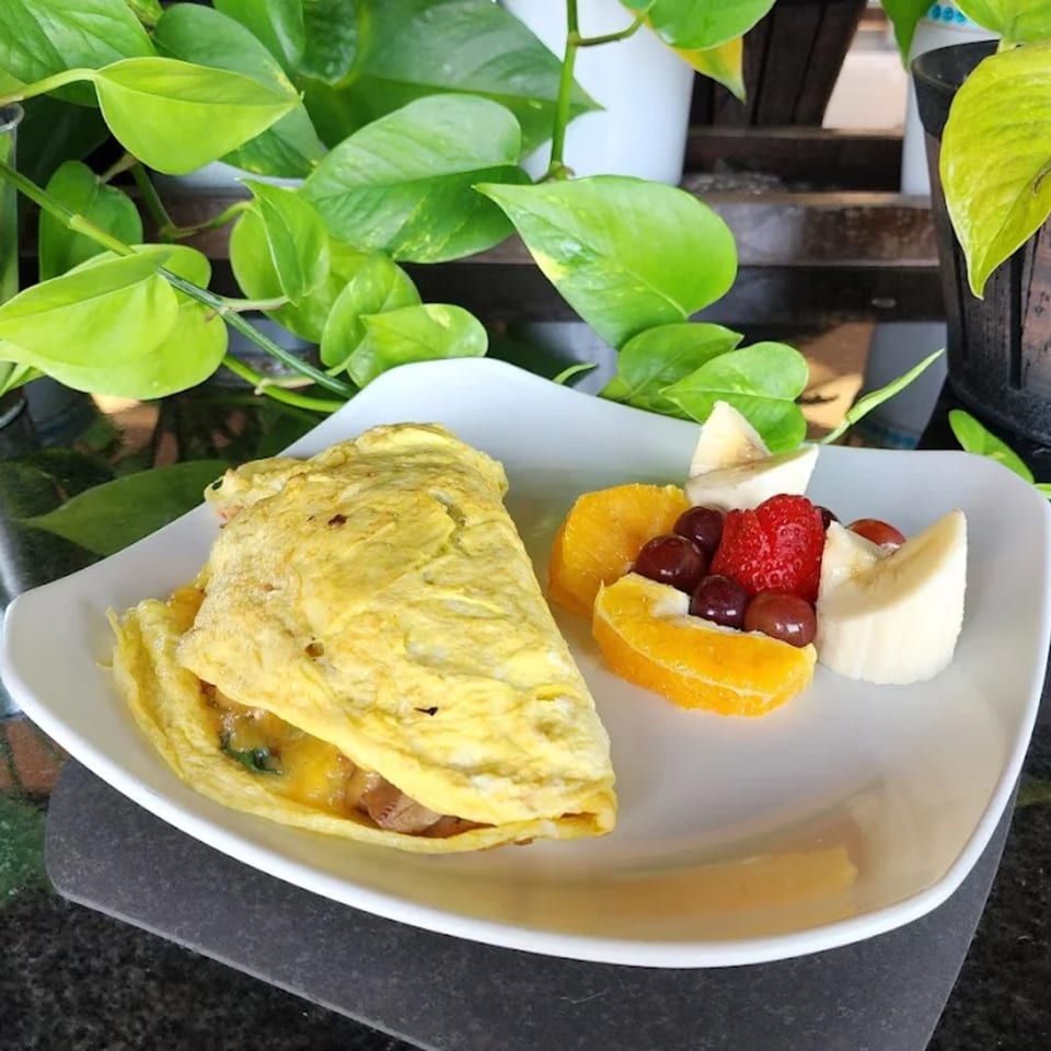 A fluffy omelet with a side of fresh fruit including oranges, strawberries, grapes, and bananas.