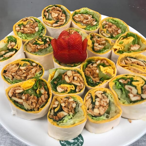 A white platter filled with numerous chicken and lettuce wraps, garnished with a strawberry.