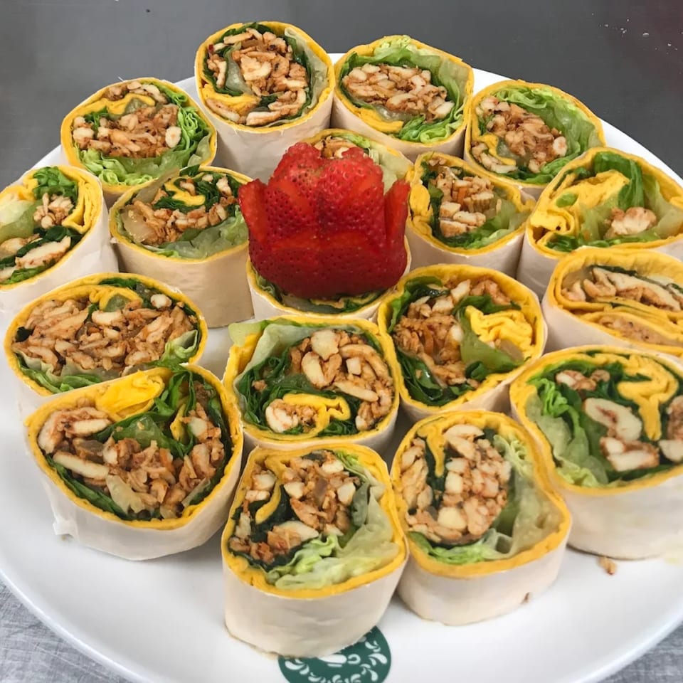 A white platter filled with numerous chicken and lettuce wraps, garnished with a strawberry.