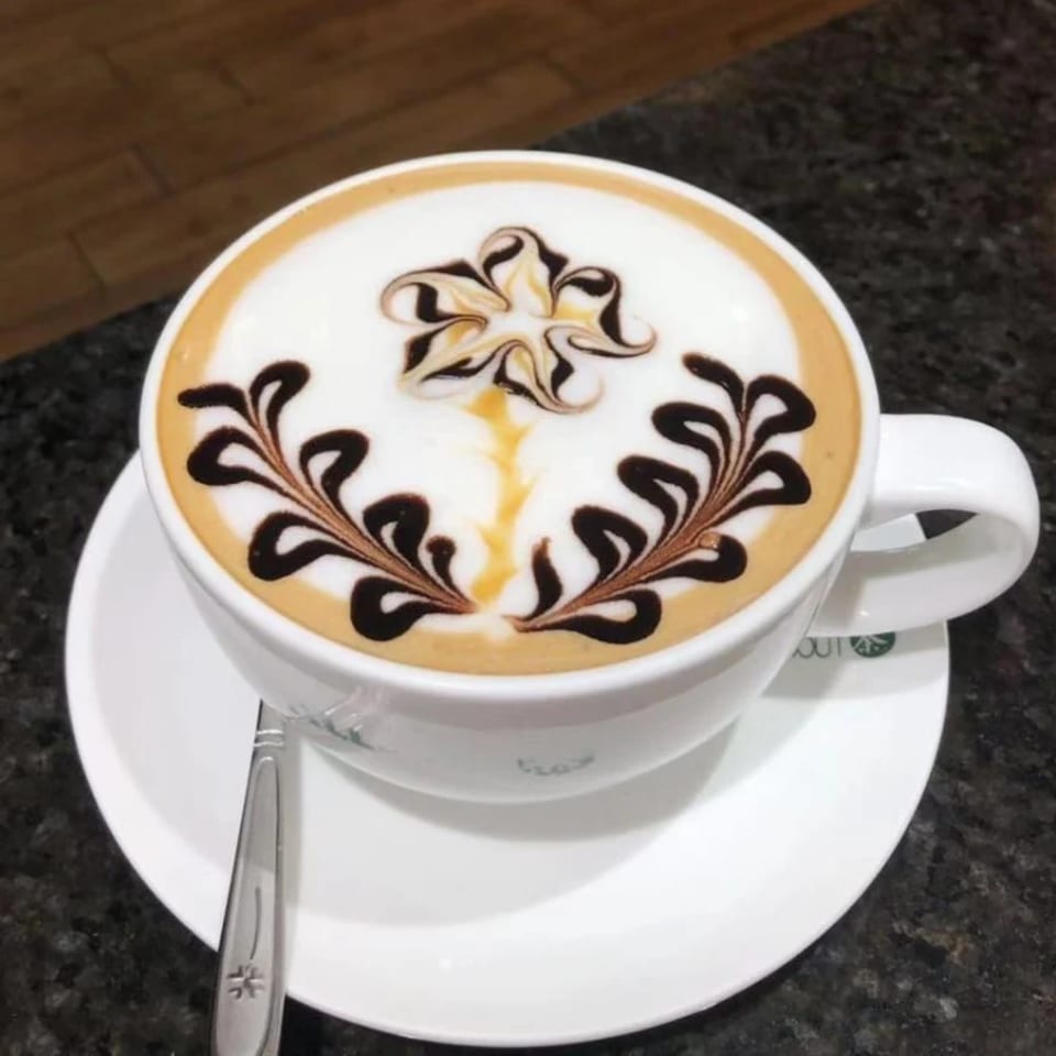 A white cup of latte art with chocolate and caramel designs on a white saucer.
