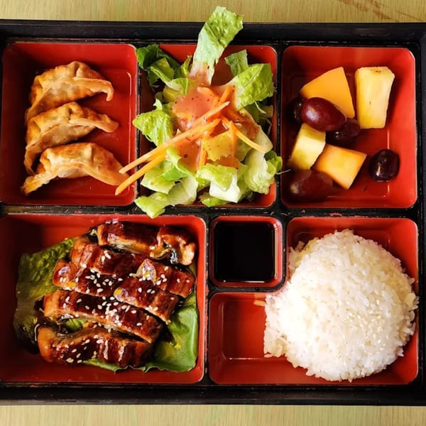 A bento box with teriyaki eel, rice, dumplings, salad, and fruit from All About Cha Cafe.
