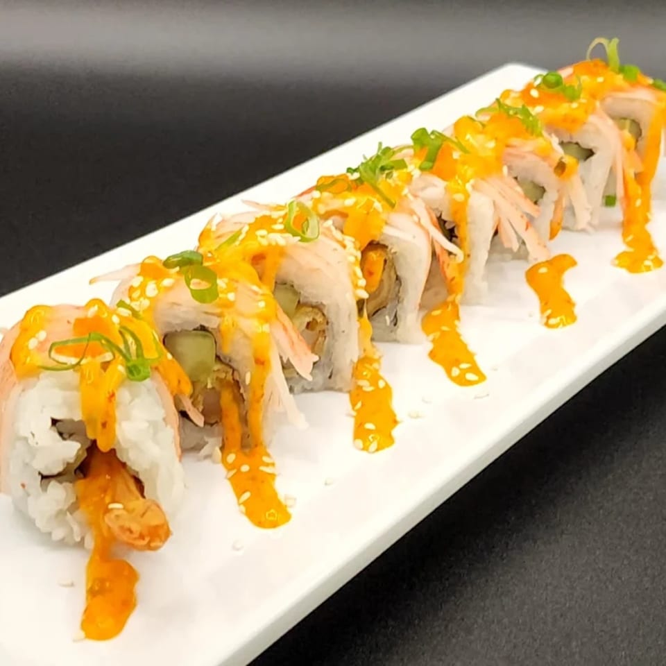 A row of sushi rolls with orange sauce, sesame seeds, and green onions on a white plate.